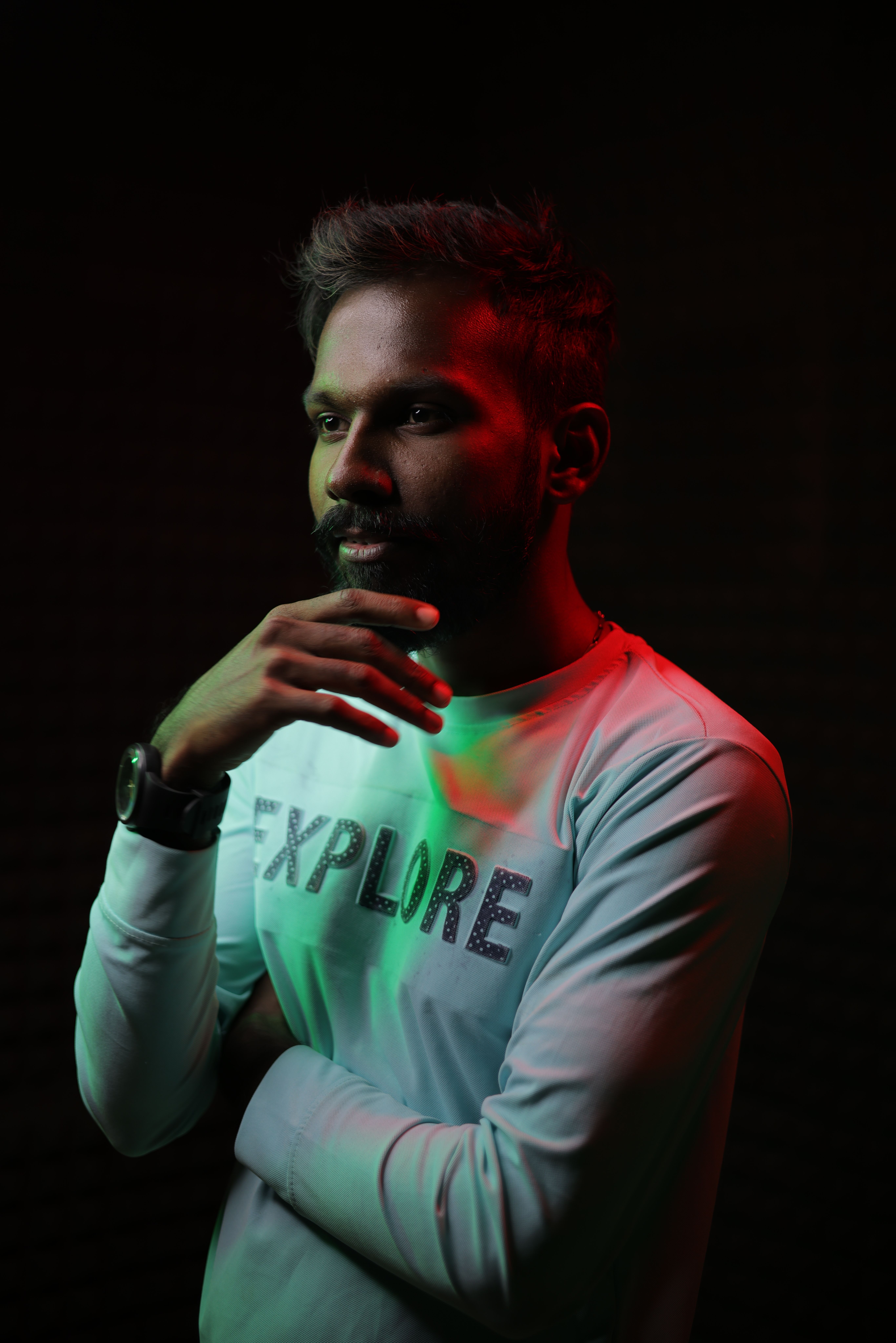 A thoughtful man in a studio wearing an 'EXPLORE' shirt, highlighted by colorful lighting.