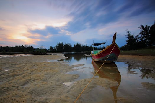 A tranquil evening scene at the beach featuring a colorful canoe and serene sunset reflection on the water.
