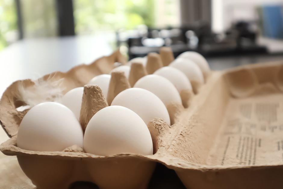 Fresh brown and white eggs in cardboard carton on wooden surface