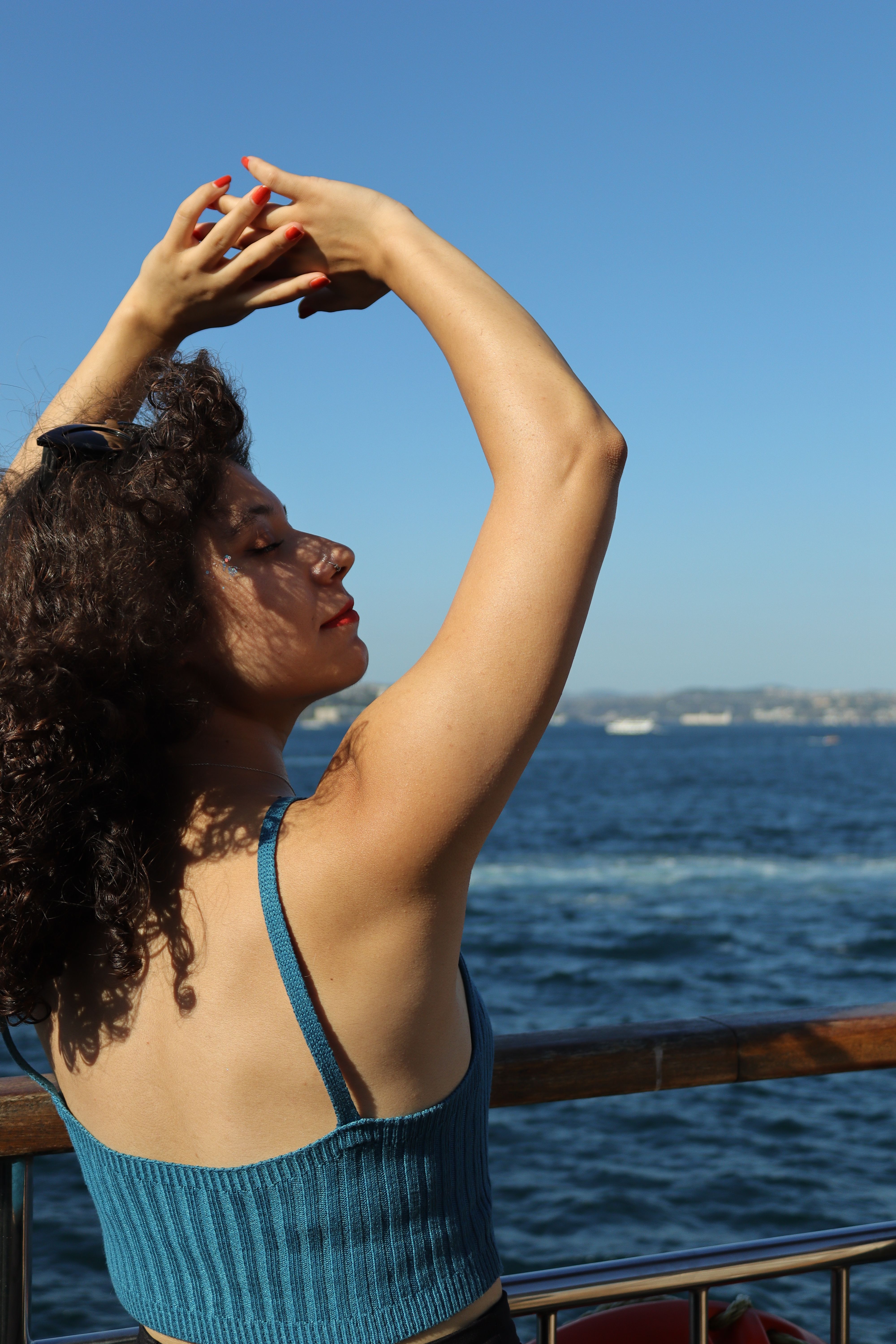 Woman with curly hair standing on a ferry, enjoying the sun and sea view.
