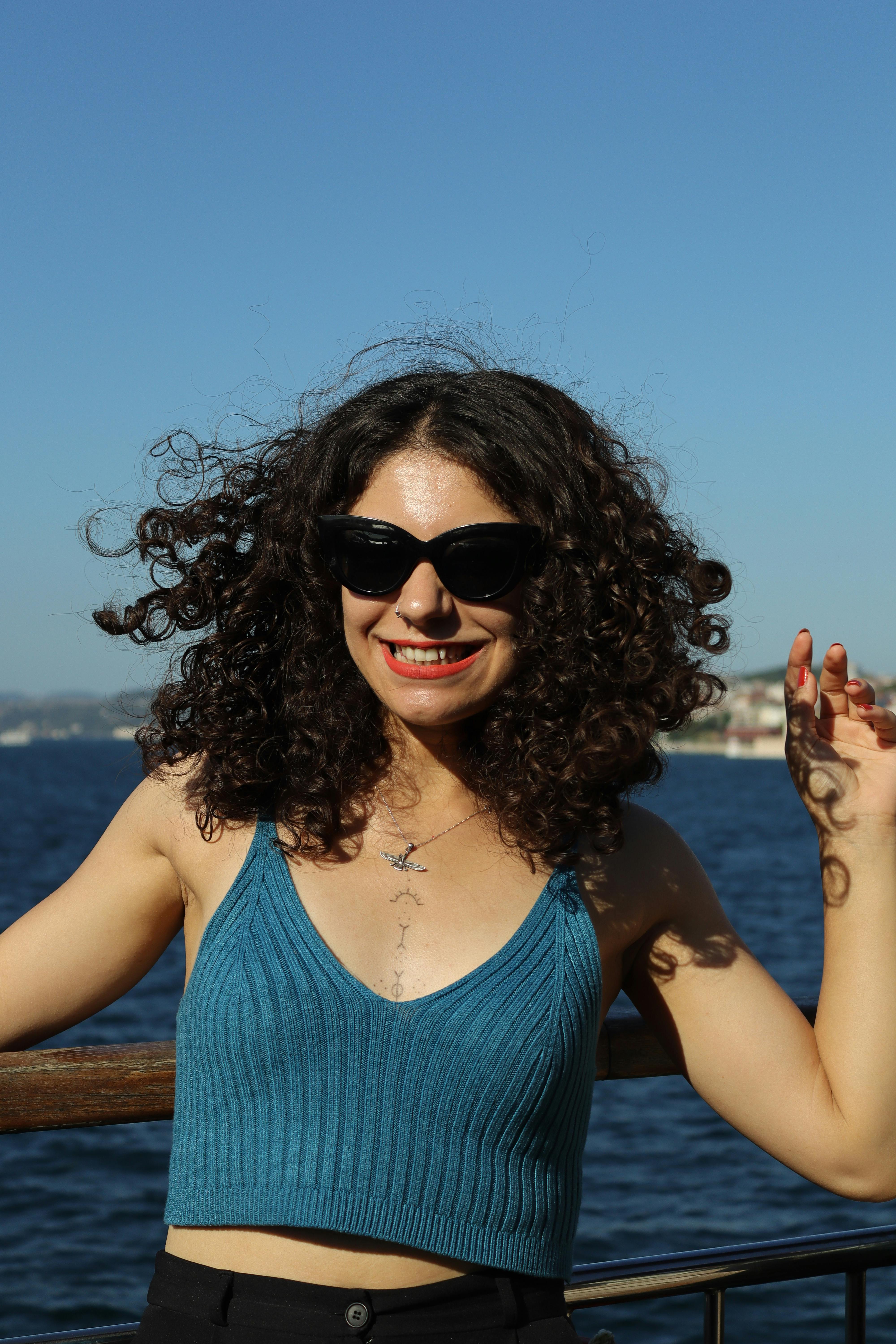 Smiling woman in sunglasses enjoying a sunny day by the sea, embodying summer fun.