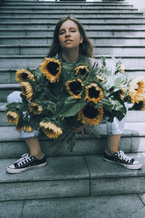 Young Woman Sitting on Steps in City with a Bunch of Sunflowers