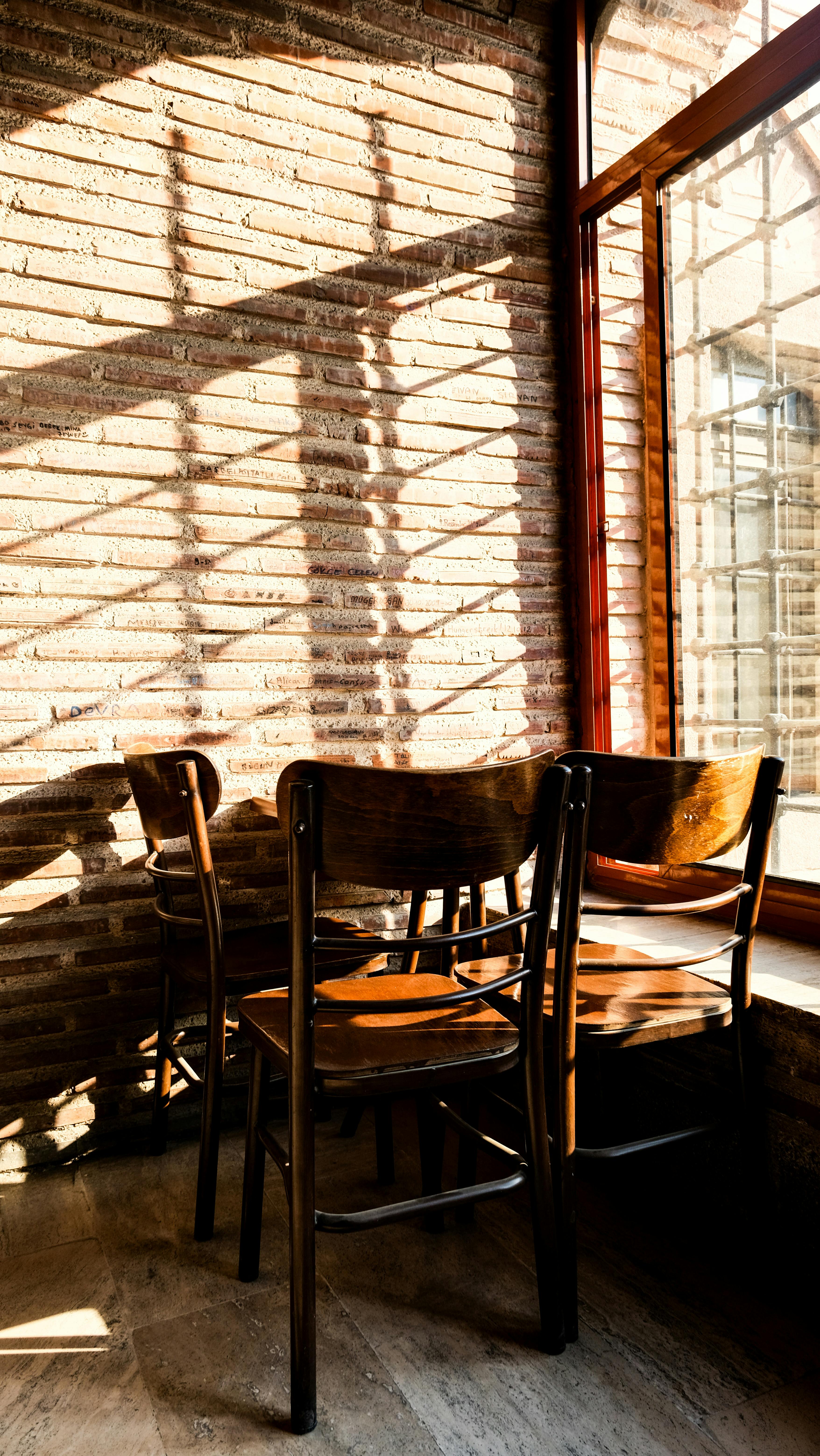 Free Inviting sunlit corner with wooden chairs and brick walls, perfect for a relaxing atmosphere. Stock Photo