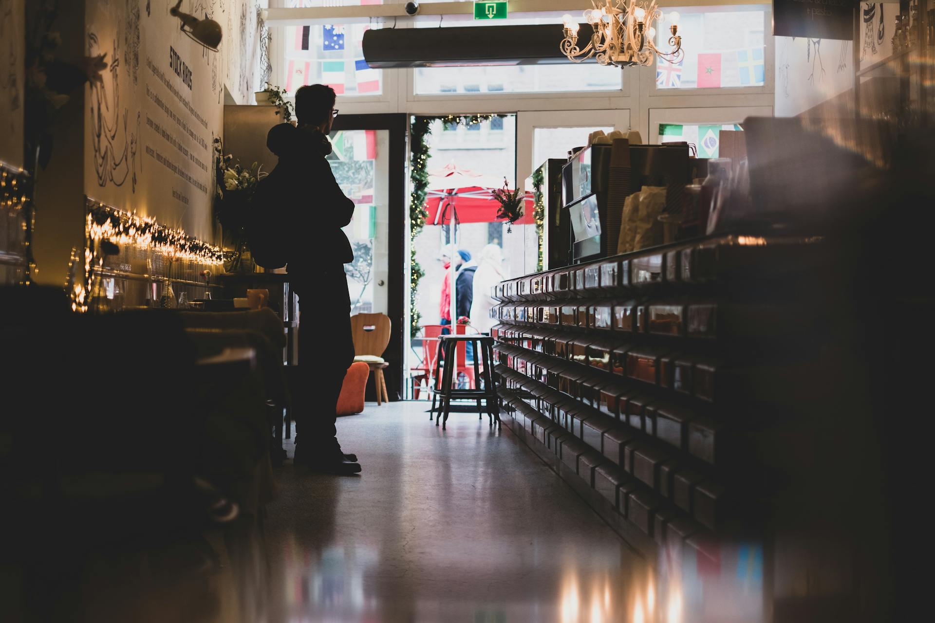 A man in silhouette stands inside a cozy shop in Amsterdam, with soft lighting and an inviting atmosphere.