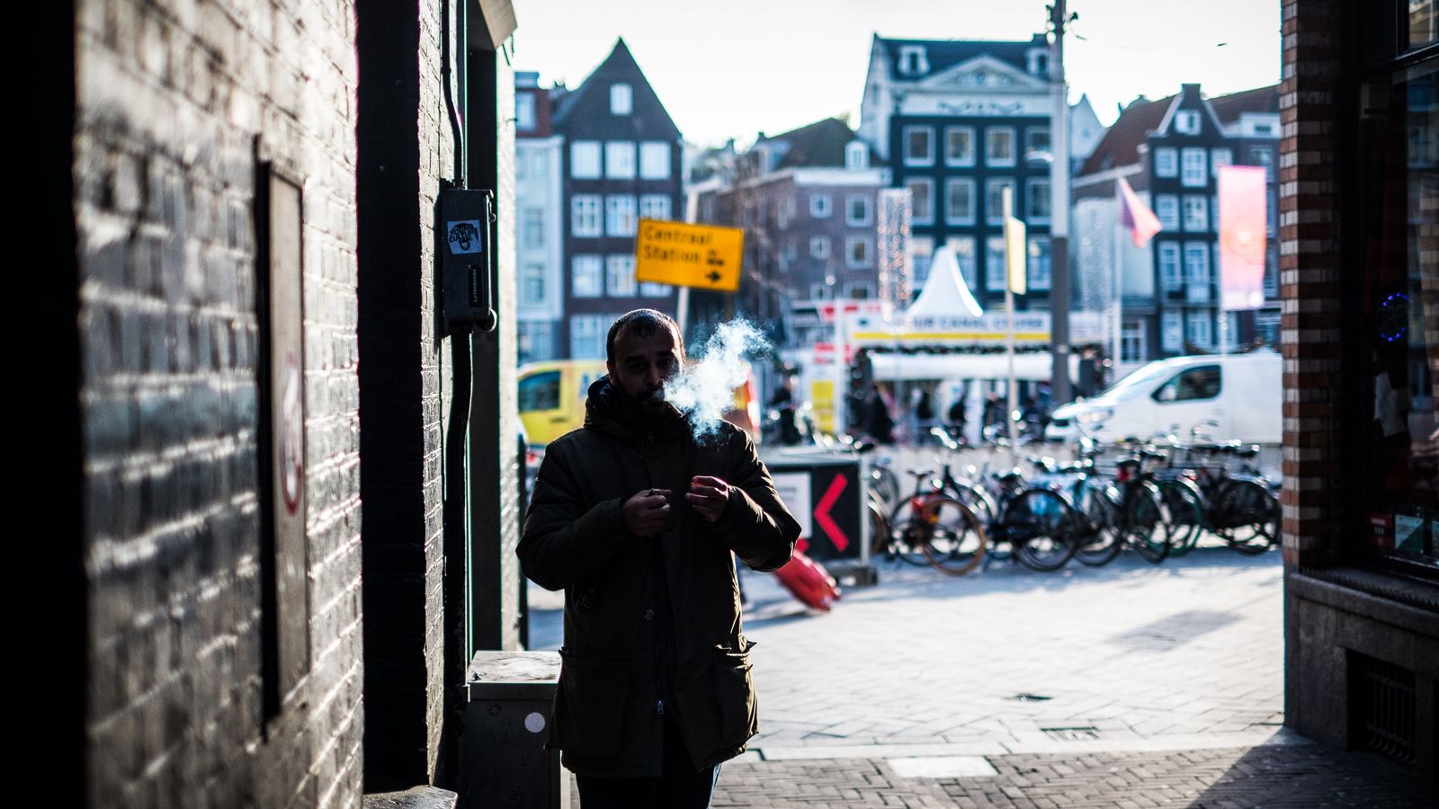 A man smokes in a vibrant Amsterdam street scene with bicycles and architecture.