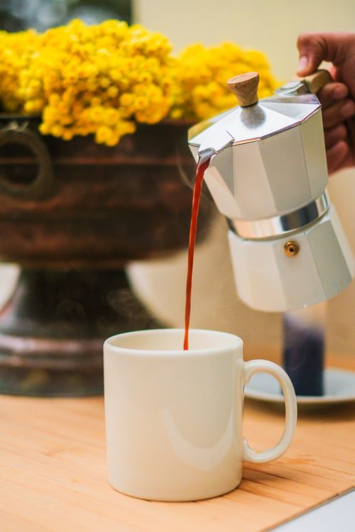 Free Close-up of hot coffee being poured from a moka pot into a white mug indoors. Stock Photo