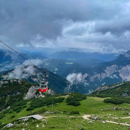 Free A red cable car traverses the lush Bavarian Alps under a cloudy sky. Stock Photo