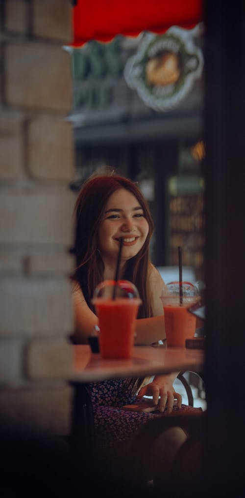 Smiling Young Woman Sitting with a Smoothie at a Table in a Cafe