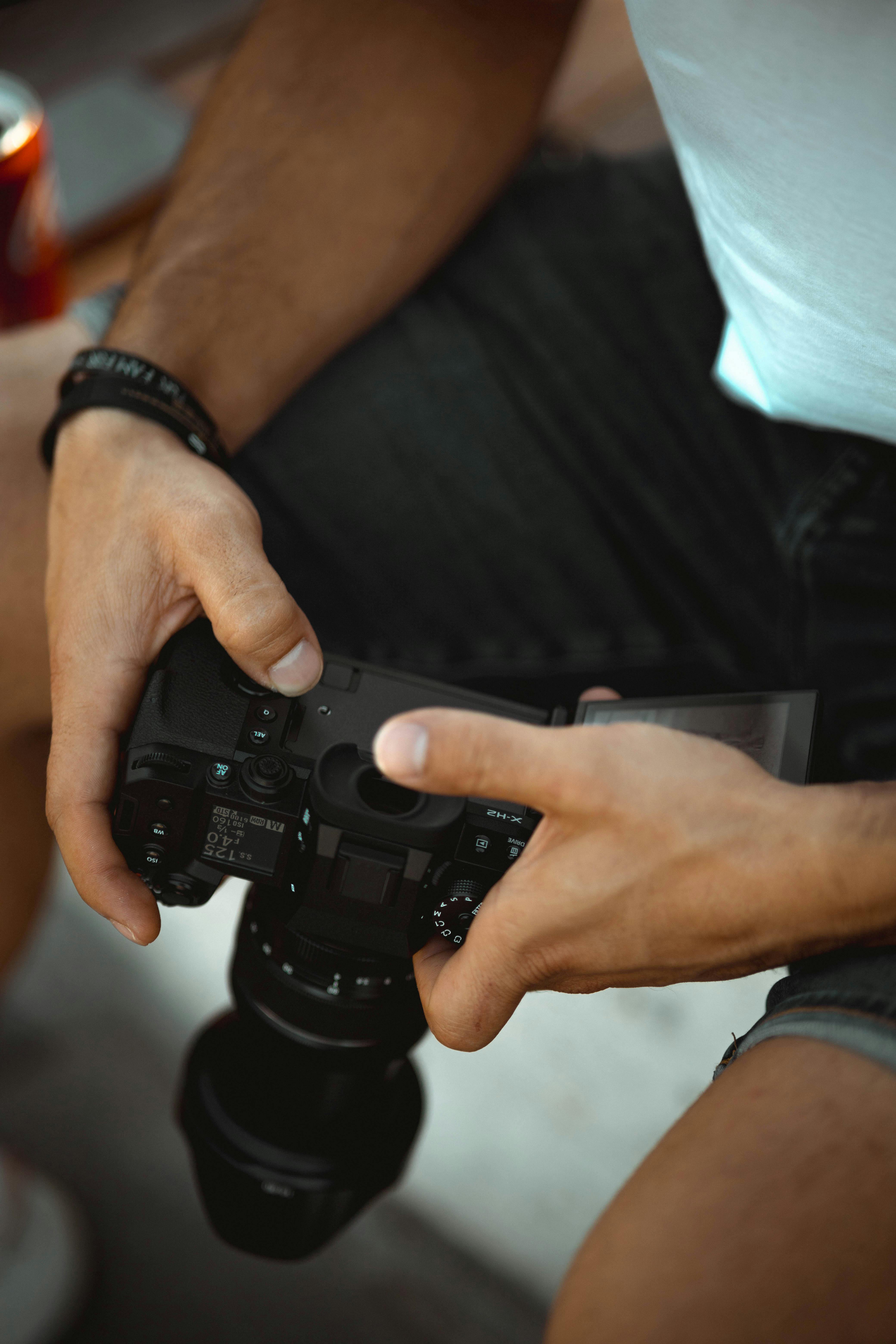 Free A photographer's hands holding and adjusting a digital camera during a photo shoot. Stock Photo