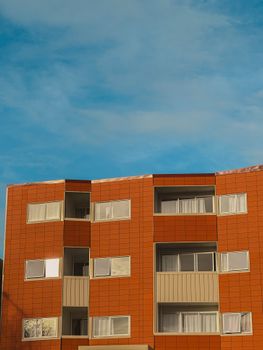 Contemporary low-rise apartment building with red exterior and balconies against blue sky.