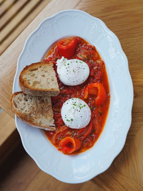 Free Delicious poached eggs served on a vibrant tomato and pepper base with rustic bread slices. Stock Photo