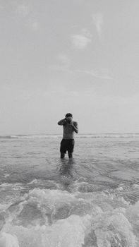 Photographer standing in the ocean, capturing the horizon in a striking black and white image.