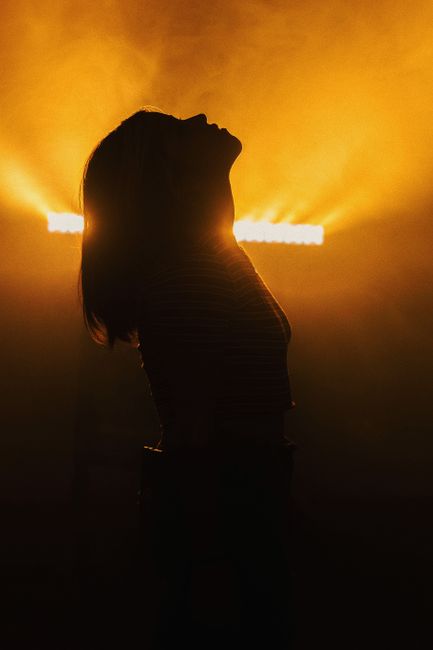 A striking silhouette of a woman with her head back, illuminated by backlit golden lights in a contemporary setting.