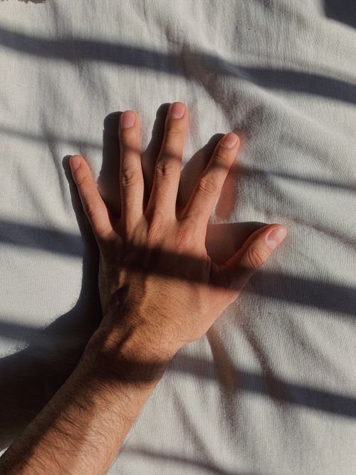 Free A man's hand resting on a sunlit white sheet, casting soft shadows. Stock Photo