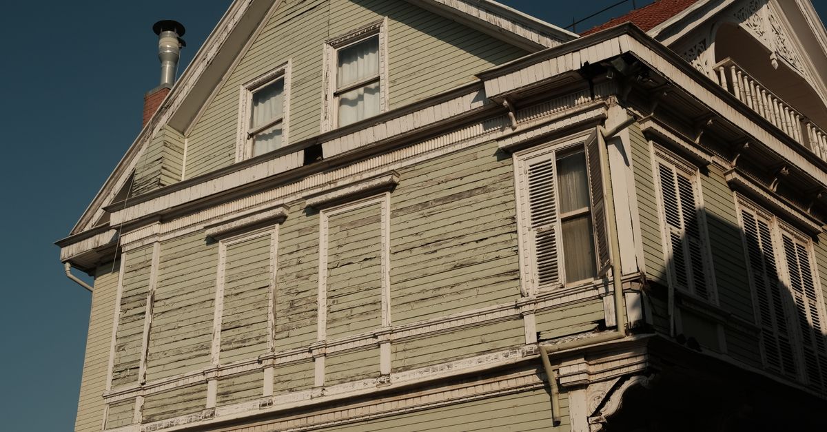 A charming vintage wooden house bathed in sunlight, showcasing its rustic green facade and intricate details.