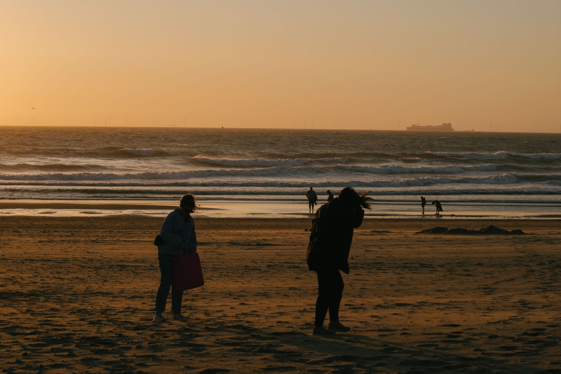 Silhouetted people enjoy a stunning sunset at Scheveningen Beach in The Hague, Netherlands.