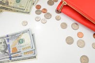 白色表面上，散落着美国纸币和硬币的俯视图，旁边放着一个红色钱包