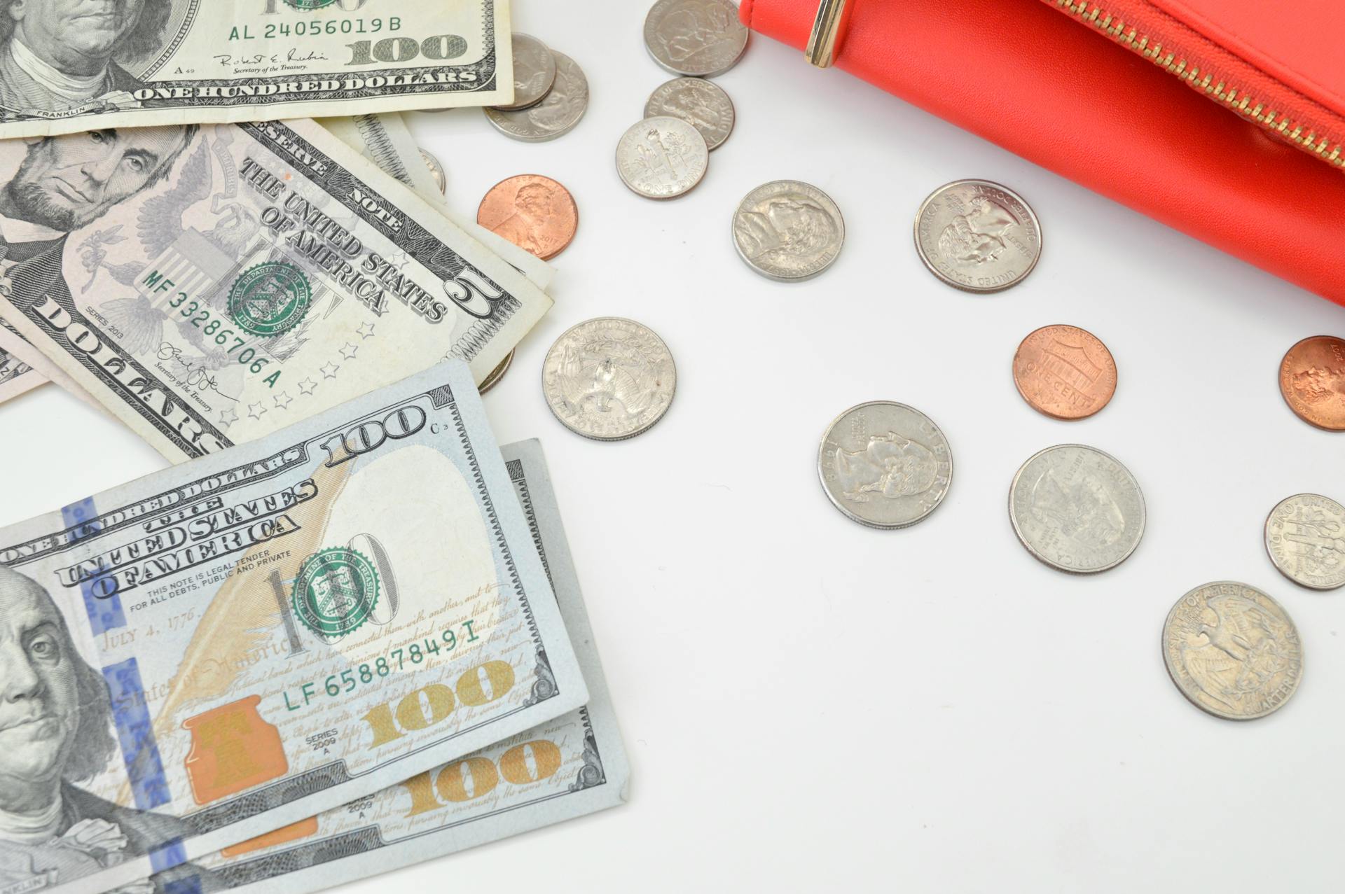 Detailed image of US dollars and coins spread with a red wallet on a white surface, ideal for financial concepts.