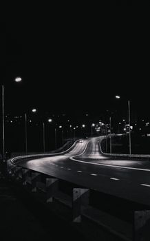 Black and white image of a quiet urban expressway at night illuminated by streetlights.