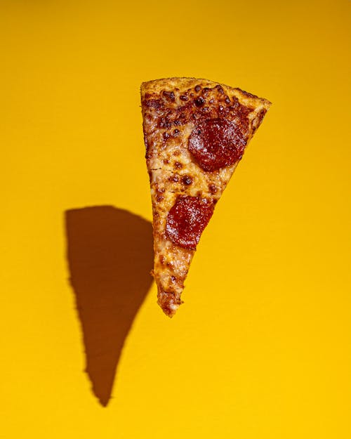 Slice of Pepperoni Pizza in Midair over Yellow Background