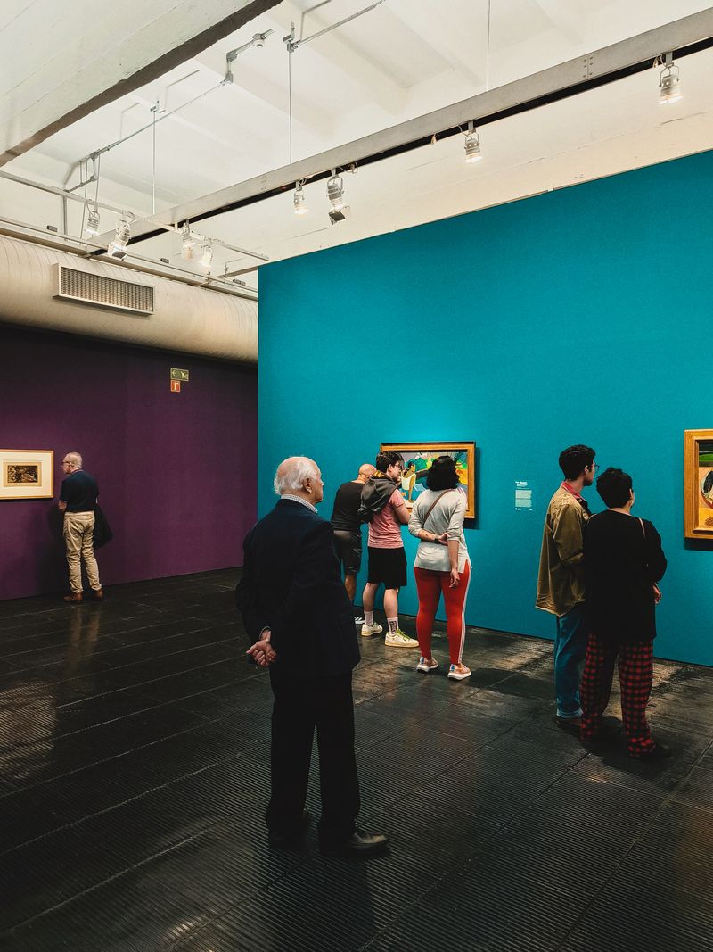 Visitors standing in an art gallery looking at paintings displayed on colorful walls in a museum interior