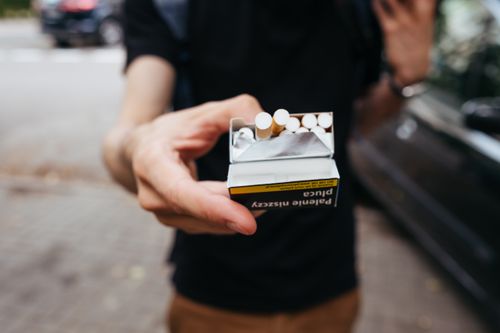 Free Close-up of a man offering a pack of cigarettes outdoors on a city street. Stock Photo