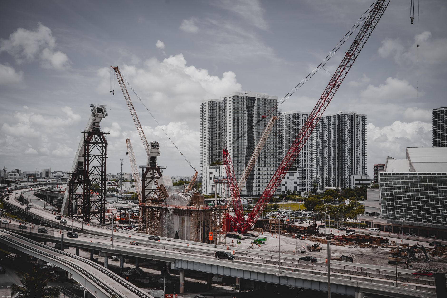A cityscape featuring high-rise buildings and a construction site with cranes under a cloudy sky.