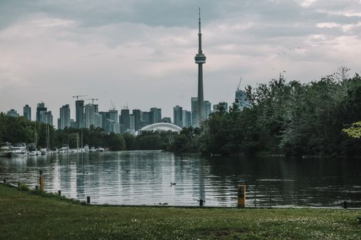 Scenic view of Toronto skyline featuring the iconic CN Tower and lush greenery on a cloudy day.