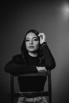 Elegant black and white portrait of a woman sitting on a chair in a studio setting.