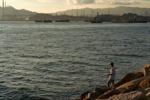 A Man Standing on the Rocky Shore and Fishing 