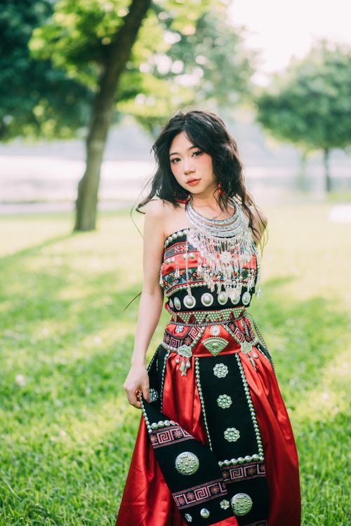 Free Beautiful woman in traditional red dress posing gracefully in a lush green park. Stock Photo
