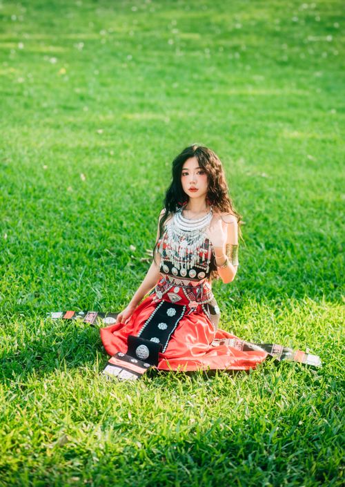 Free Portrait of a woman in traditional Asian attire sitting on green grass, showcasing cultural fashion. Stock Photo