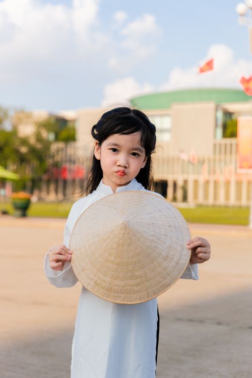 Free Asian child in traditional dress holding a hat with city buildings in the background. Stock Photo