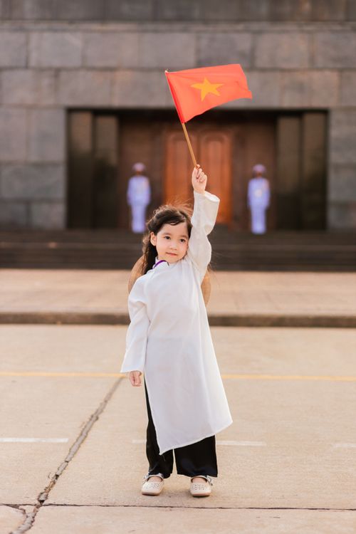 Free A child in traditional attire holds the Vietnamese flag proudly in a town square. Stock Photo