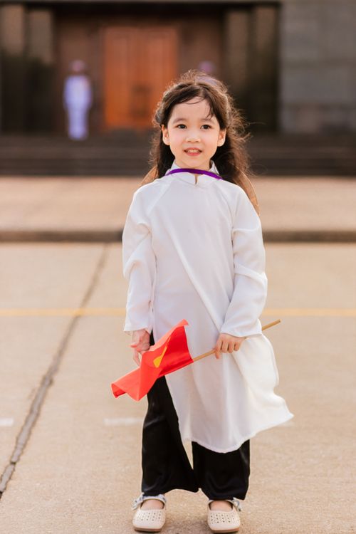 Free Young girl in traditional attire holding a red flag standing in a town square. Stock Photo