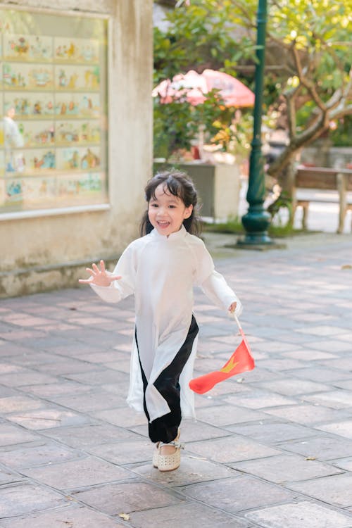 A Little Girl in a Traditional Dress Running with a Flag in Hand 