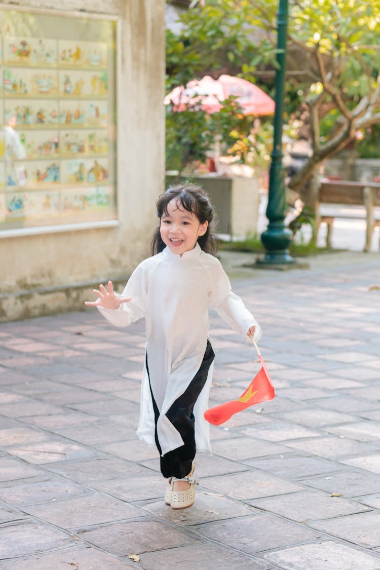 A Little Girl In A Traditional Dress Running With A Flag In Hand 