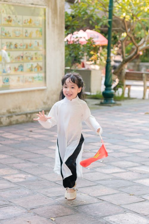 Free A young girl joyfully runs outdoors holding a flag in traditional attire, exuding happiness. Stock Photo