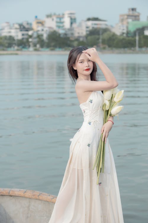 Young Woman in a White Dress Holding a Bunch of Flowers