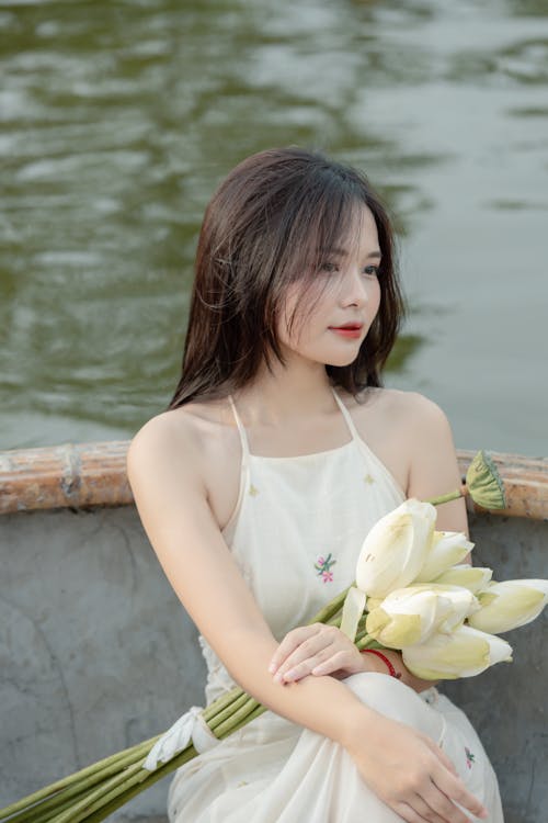 Young Woman Sitting in a Boat with a Bunch of Flowers in her Lap 