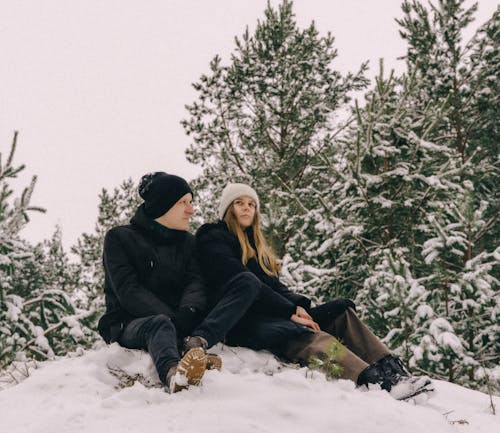 Young Couple Sitting on a Snow Covered Hill among Trees 