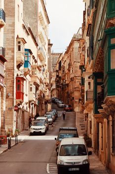 Explore the charming narrow streets of Valletta, Malta with colorful balconies and parked cars.