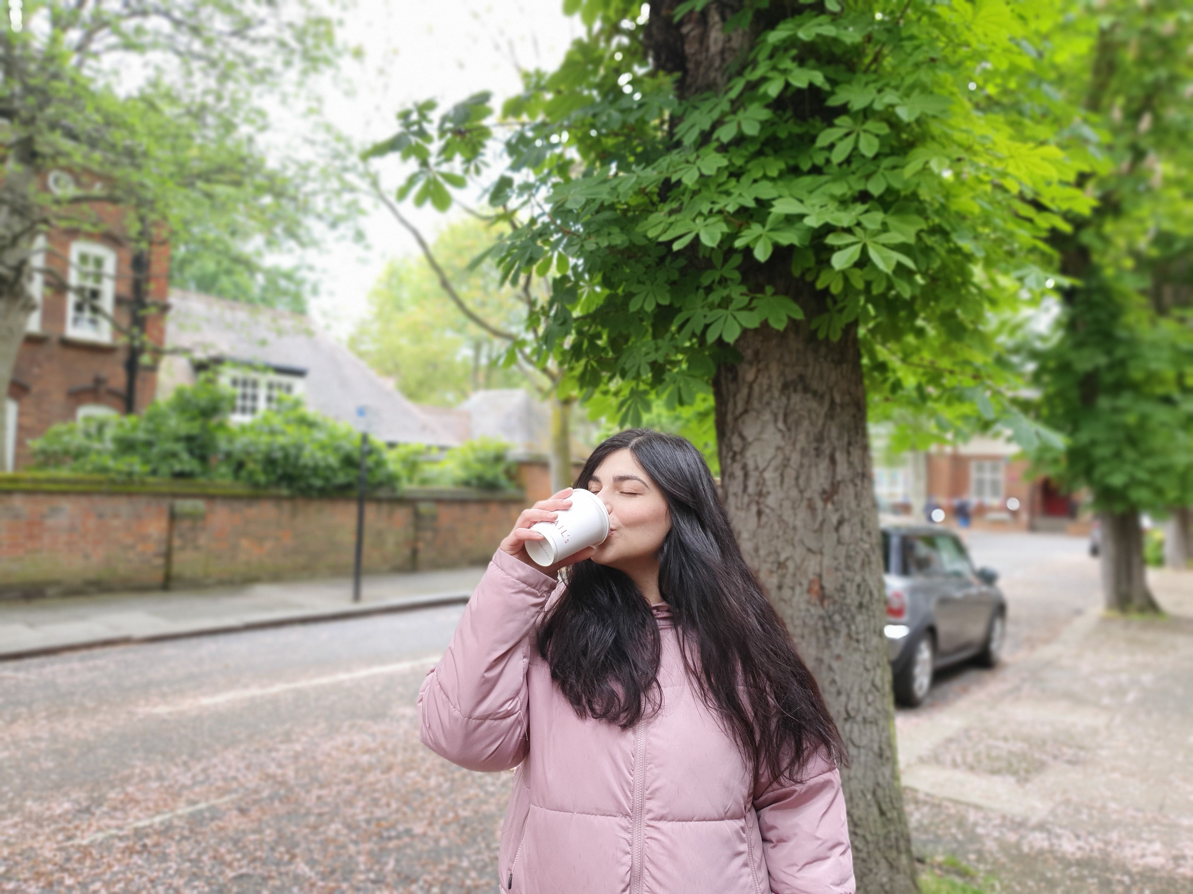 A woman in a pink jacket enjoys a warm coffee on a tranquil street in London.