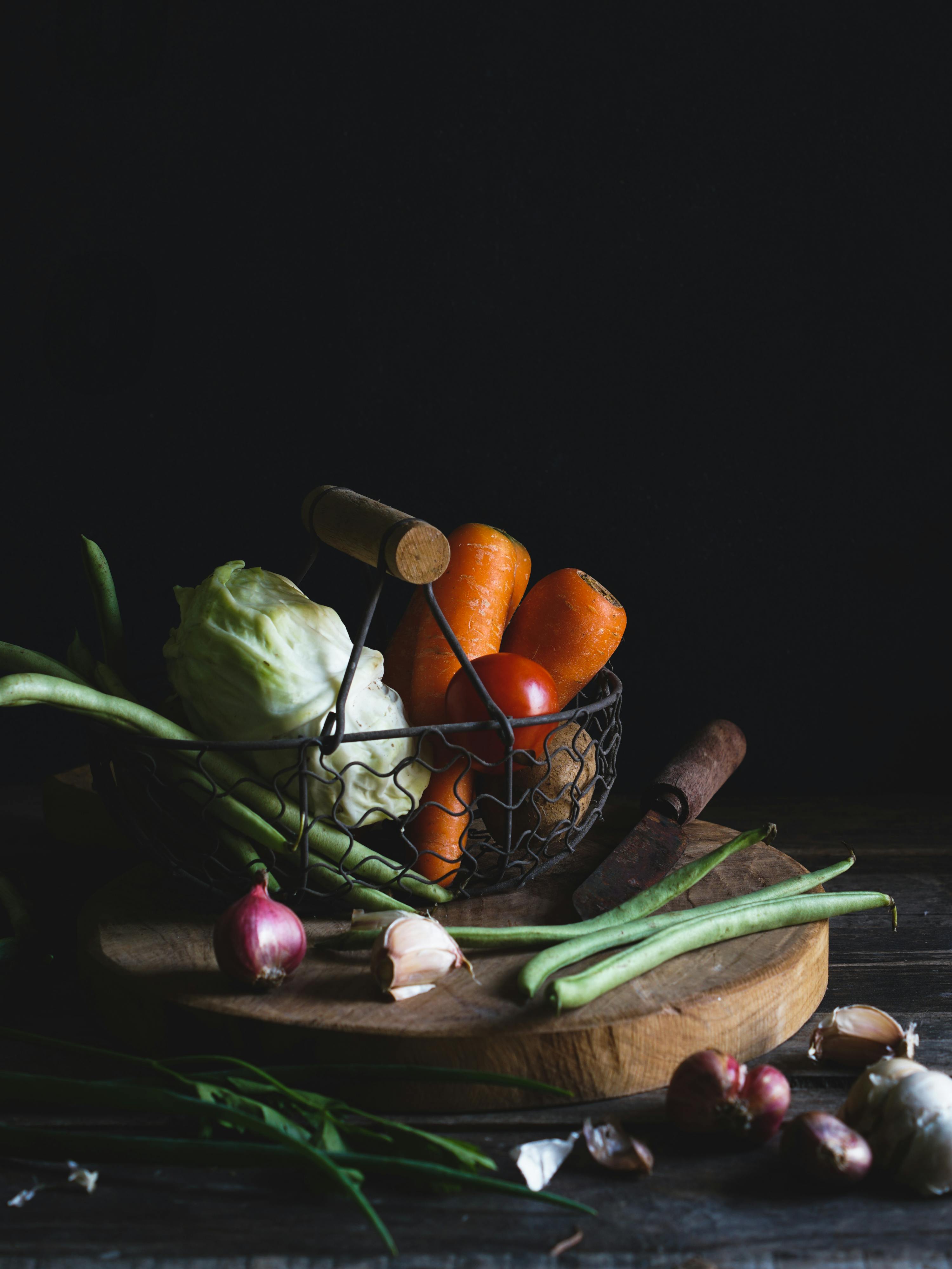A rustic basket of fresh vegetables on a wooden cutting board, perfect for food photography.