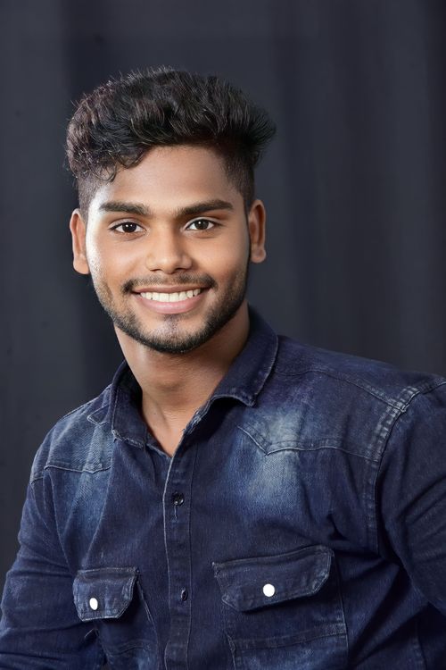 Free Cheerful young man in denim shirt posing for a portrait against dark background. Stock Photo
