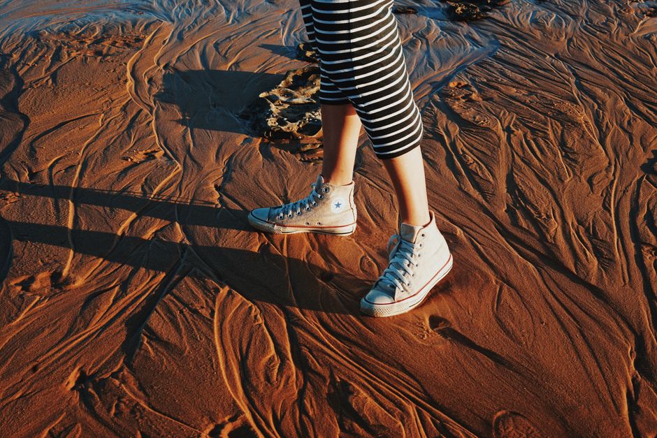 Woman wearing striped leggings and sneakers walking on a textured sandy beach at sunset.