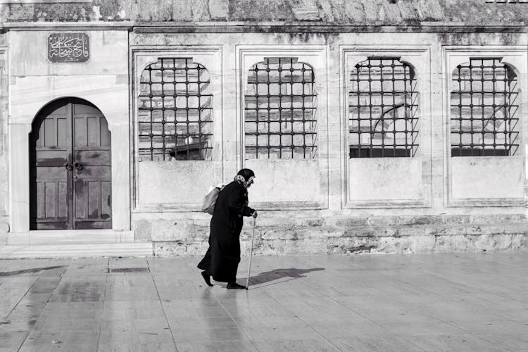 Black And White Photo Of A Woman Walking By The Building 