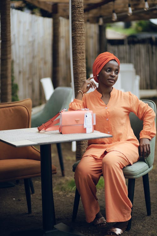 Woman in Orange Blouse, Pants and Turban Sitting at a Cafe Table