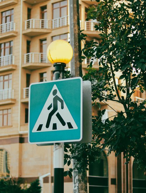 Free Close-up of an urban pedestrian sign surrounded by a residential building and greenery. Stock Photo