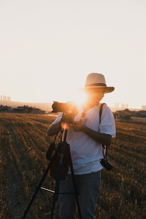 Free A photographer with a tripod in a rural field capturing the warm sunset glow. Stock Photo
